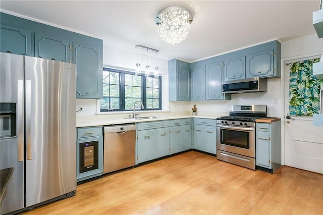 kitchen with appliances with stainless steel finishes, a sink, a chandelier, light countertops, and light wood finished floors