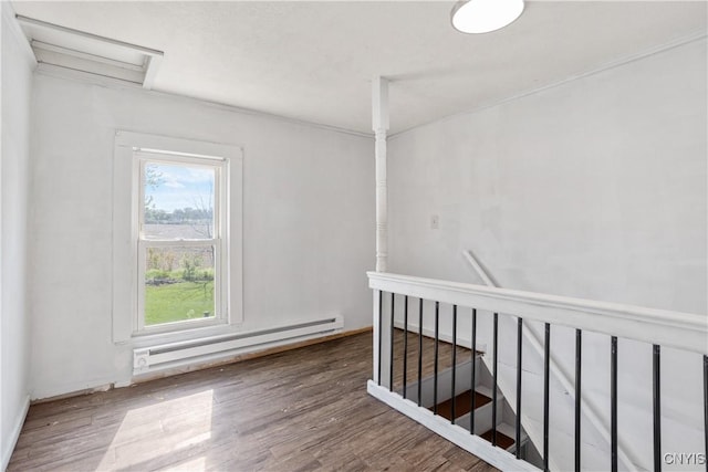 empty room featuring a baseboard radiator, wood finished floors, and attic access