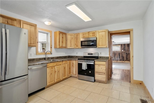 kitchen featuring appliances with stainless steel finishes, a sink, dark countertops, and light brown cabinetry