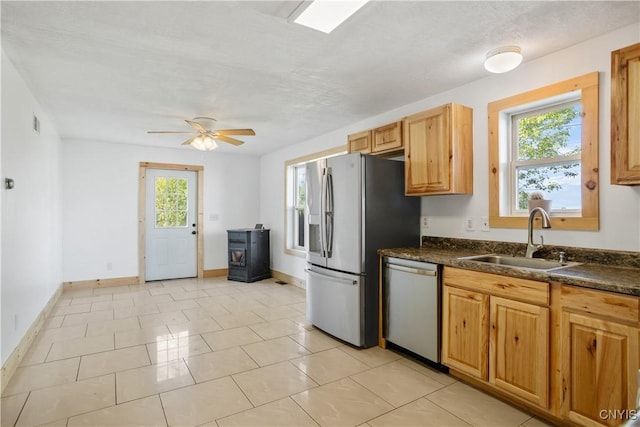 kitchen featuring stainless steel appliances, a sink, dark countertops, baseboards, and ceiling fan