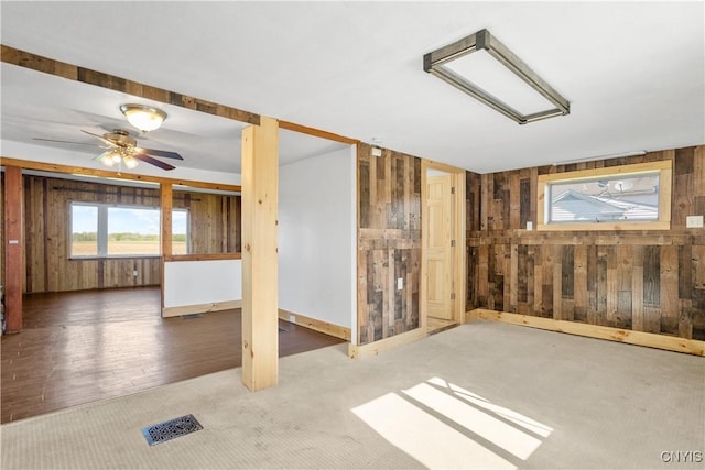 carpeted spare room featuring wooden walls and ceiling fan