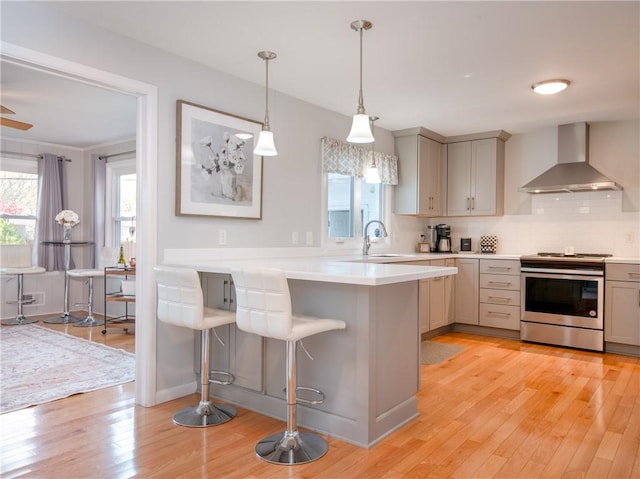 kitchen featuring wall chimney exhaust hood, electric stove, a kitchen breakfast bar, light wood-type flooring, and light countertops