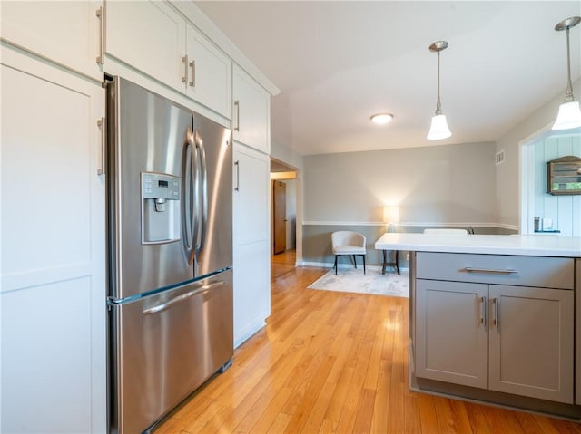 kitchen with stainless steel fridge with ice dispenser, gray cabinets, light wood-style flooring, light countertops, and hanging light fixtures