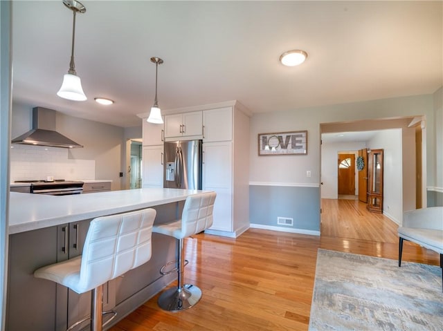 kitchen with wall chimney range hood, appliances with stainless steel finishes, light wood-style floors, and light countertops