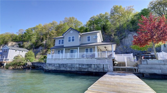 rear view of house featuring ceiling fan, a water view, and view of wooded area