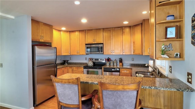 kitchen with stainless steel appliances, a sink, a peninsula, open shelves, and dark stone counters