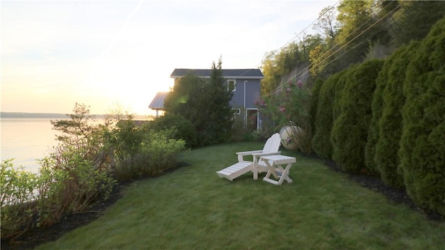yard at dusk with a lawn and a water view
