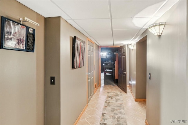 corridor with a drop ceiling, baseboards, and light tile patterned floors