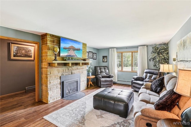 living area with baseboard heating, wood finished floors, a stone fireplace, and baseboards