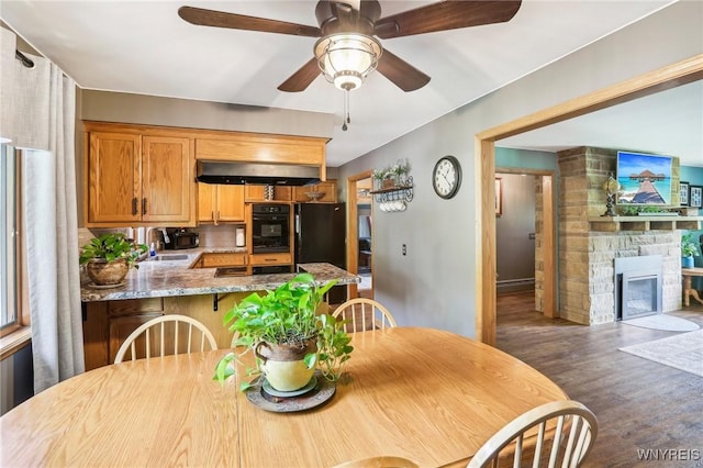dining area with wood finished floors, a ceiling fan, and a stone fireplace