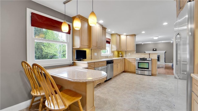 kitchen with appliances with stainless steel finishes, a peninsula, a sink, light brown cabinets, and decorative backsplash