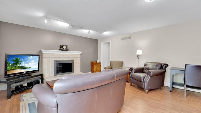 living room featuring track lighting, light wood finished floors, and a glass covered fireplace