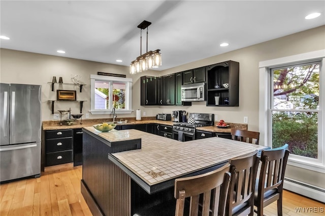 kitchen featuring appliances with stainless steel finishes, dark cabinetry, light countertops, a sink, and a kitchen island
