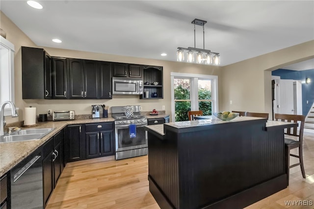 kitchen featuring appliances with stainless steel finishes, a sink, dark cabinetry, light countertops, and a kitchen island