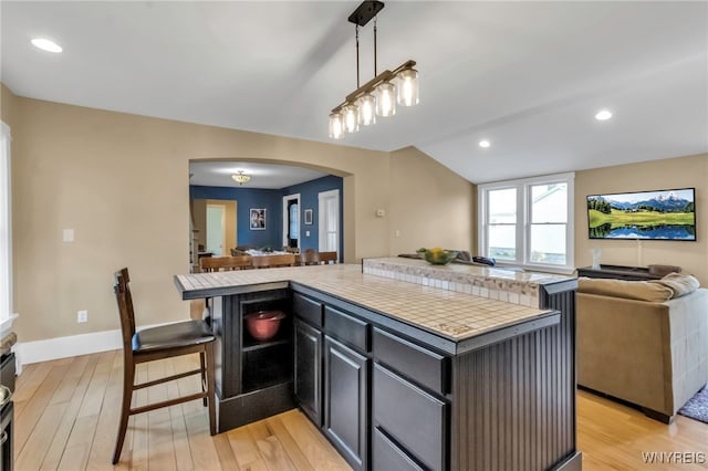 kitchen with open floor plan, arched walkways, light wood-type flooring, vaulted ceiling, and tile counters