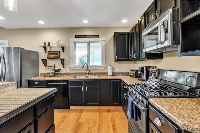 kitchen with stainless steel appliances, a sink, dark cabinetry, light countertops, and recessed lighting