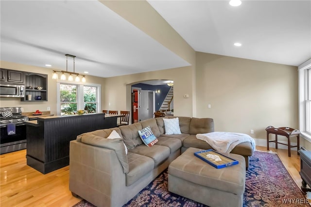 living area with arched walkways, light wood-style flooring, stairway, and recessed lighting