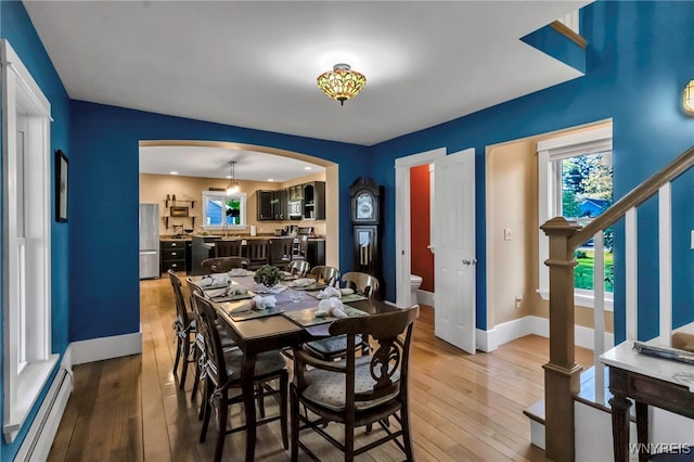 dining room featuring baseboard heating, arched walkways, light wood finished floors, and baseboards