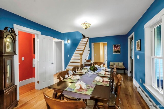 dining room with a baseboard heating unit, stairway, wood finished floors, and baseboards