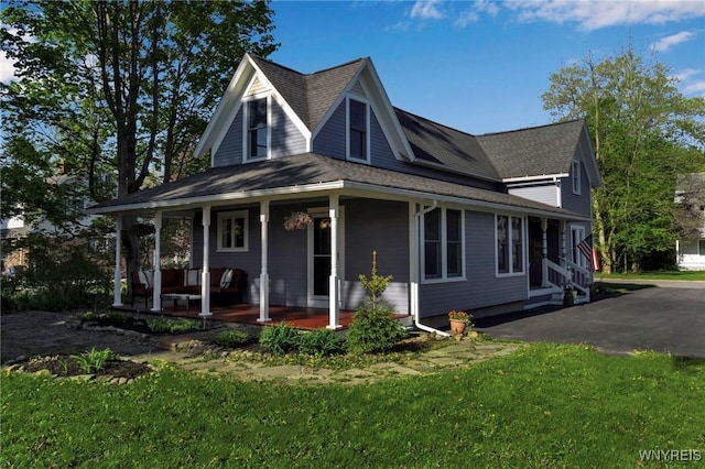 farmhouse-style home with a porch, a front yard, and a shingled roof