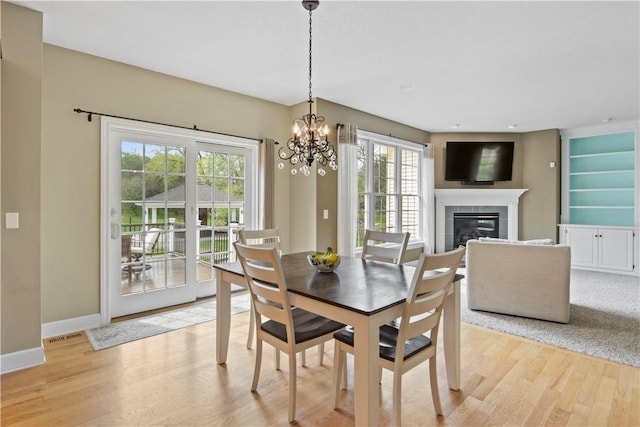 dining space with a tiled fireplace, light wood-style floors, a chandelier, and baseboards