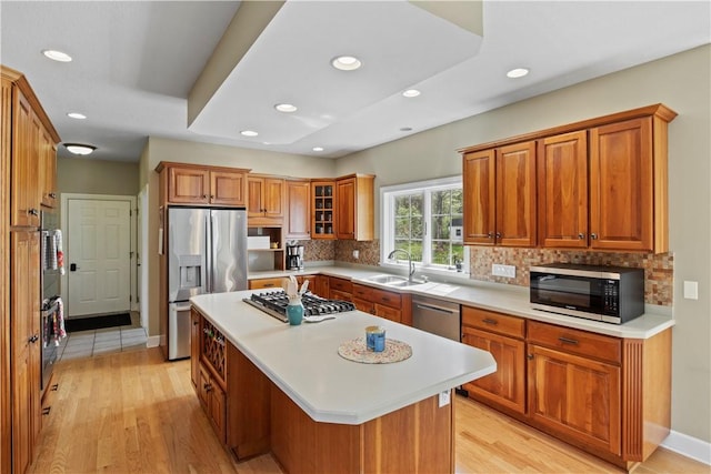 kitchen featuring appliances with stainless steel finishes, a sink, tasteful backsplash, brown cabinetry, and light wood-type flooring