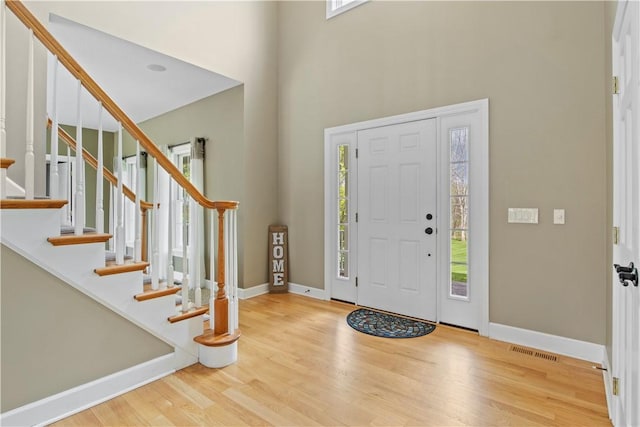 foyer entrance with a towering ceiling, wood finished floors, baseboards, and stairs
