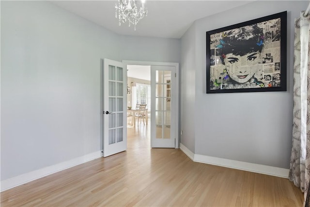 unfurnished room featuring french doors, wood finished floors, a chandelier, and baseboards
