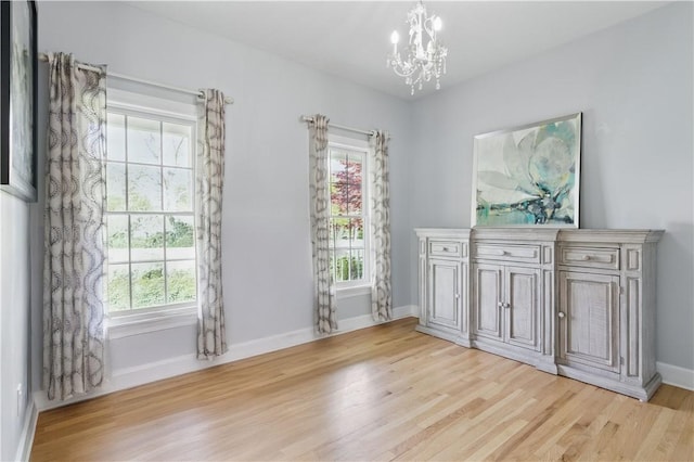 unfurnished room with a chandelier, light wood-style floors, and baseboards