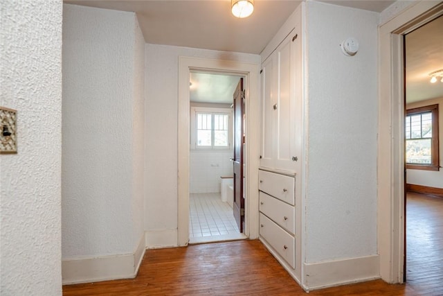 corridor featuring healthy amount of natural light, wood finished floors, and baseboards