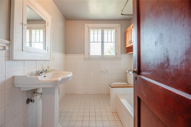 bathroom featuring tile walls, tile patterned floors, wainscoting, a bath, and toilet