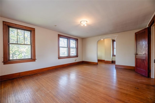 spare room featuring arched walkways, light wood-type flooring, and baseboards