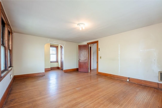spare room with arched walkways, light wood-style floors, and baseboards
