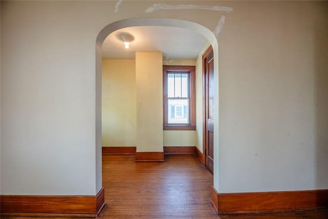 hallway with arched walkways, wood finished floors, and baseboards