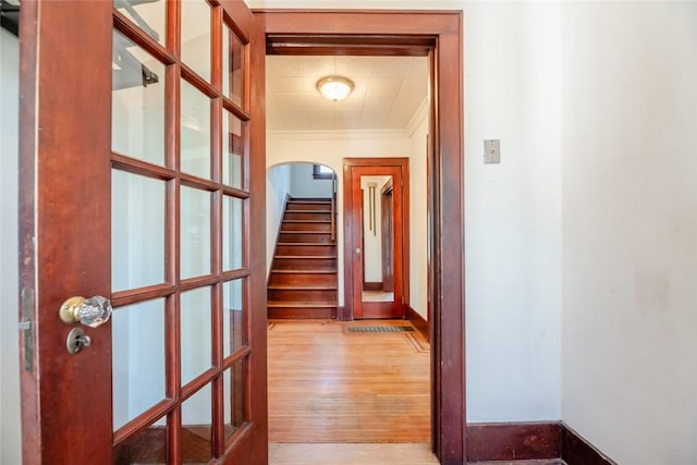 hallway with wood finished floors, crown molding, arched walkways, and baseboards