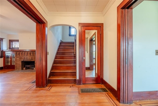 stairs with wood finished floors, a brick fireplace, arched walkways, ornamental molding, and baseboards