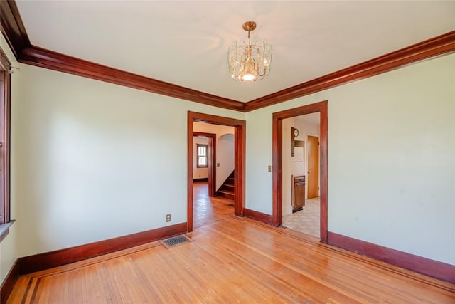 empty room with crown molding, light wood-type flooring, a chandelier, baseboards, and stairway