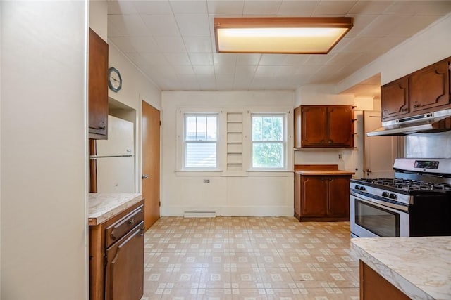 kitchen with under cabinet range hood, stainless steel range with gas cooktop, light countertops, freestanding refrigerator, and brown cabinetry