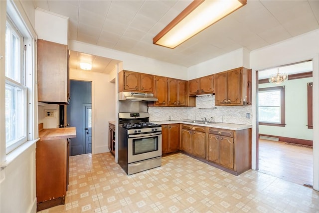 kitchen with stainless steel gas range, under cabinet range hood, light countertops, brown cabinets, and tasteful backsplash
