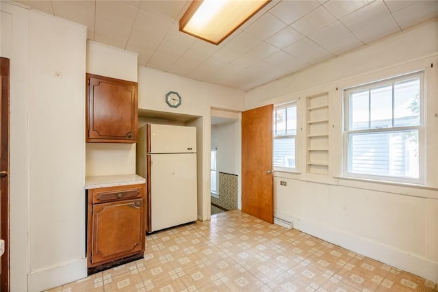 kitchen featuring freestanding refrigerator, light countertops, brown cabinetry, and built in features
