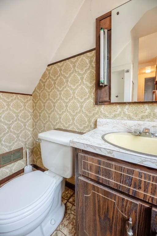 bathroom featuring wallpapered walls, lofted ceiling, toilet, and vanity