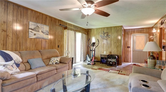living area with wooden walls, a ceiling fan, crown molding, and carpet flooring