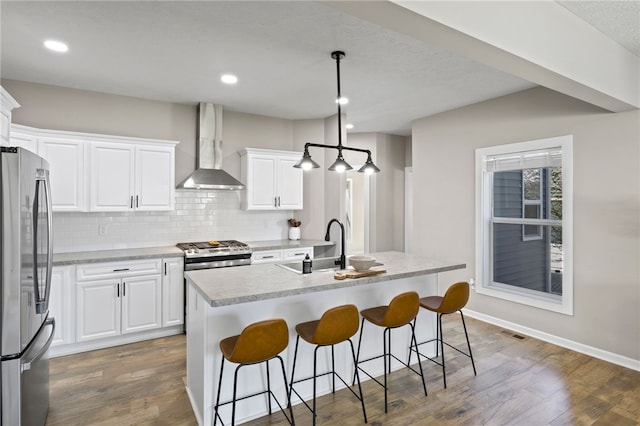 kitchen featuring stainless steel appliances, wall chimney exhaust hood, a sink, backsplash, and light countertops