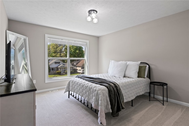 bedroom featuring light carpet, baseboards, and a textured ceiling