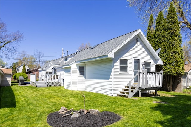 rear view of house with a shingled roof, a wooden deck, and a yard