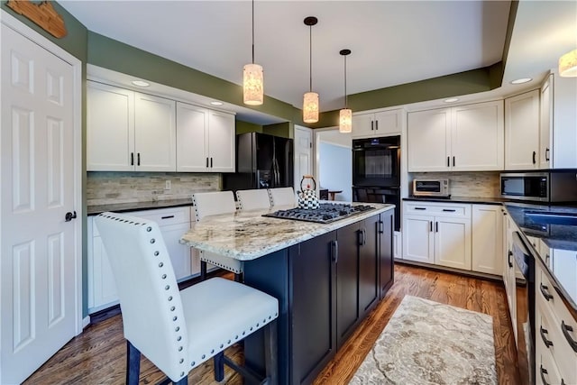 kitchen featuring black appliances, decorative backsplash, a kitchen island, a breakfast bar, and recessed lighting