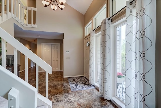 foyer entrance with stairs, high vaulted ceiling, baseboards, a chandelier, and stone finish floors