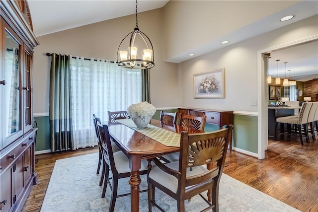 dining space featuring a chandelier, wood finished floors, vaulted ceiling, baseboards, and recessed lighting