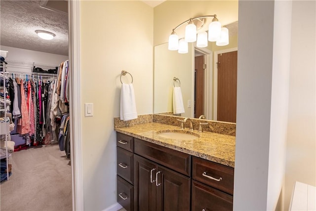 bathroom with vanity, a walk in closet, and a textured ceiling