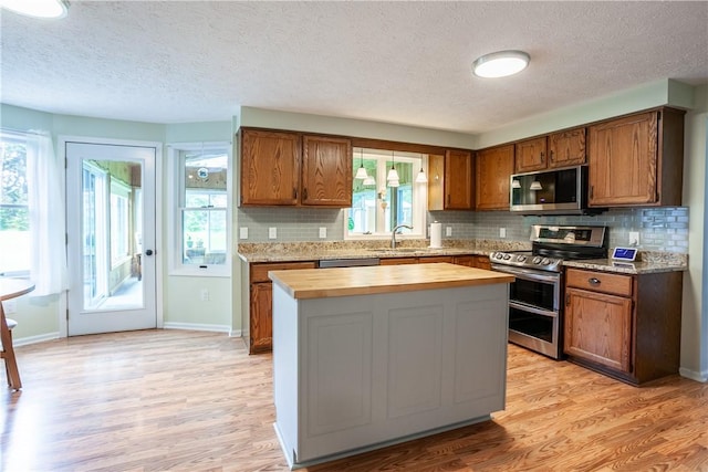 kitchen with appliances with stainless steel finishes, a textured ceiling, a sink, wood counters, and brown cabinetry